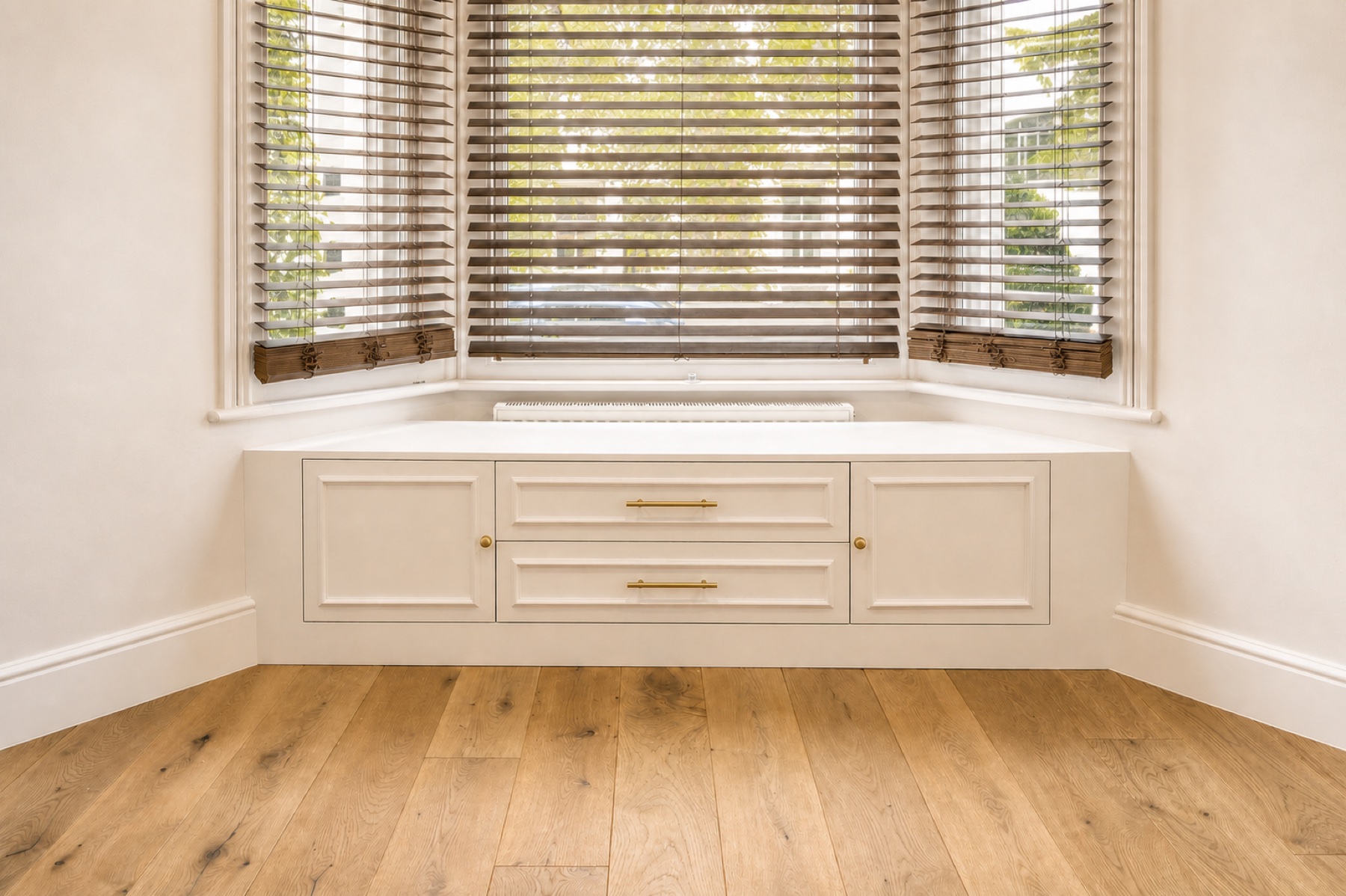 Completed London bay window with warm-white fitted storage, brass hardware, timber blinds and oak flooring