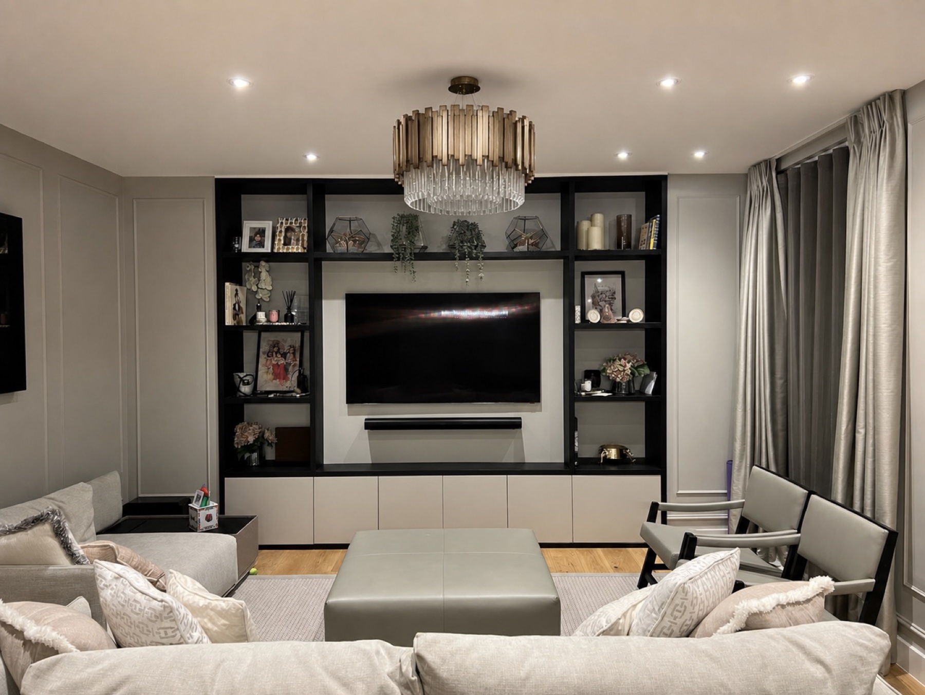 Completed London living room with black bespoke media joinery, pale seating and a tiered chandelier