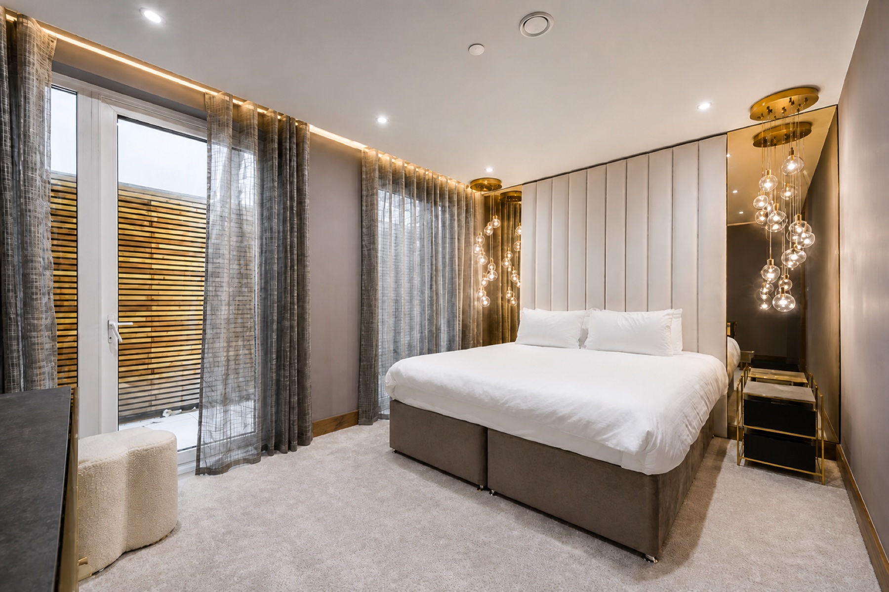 Completed London bedroom with a full-height upholstered headboard, bronze mirrors and cascading glass pendant lights